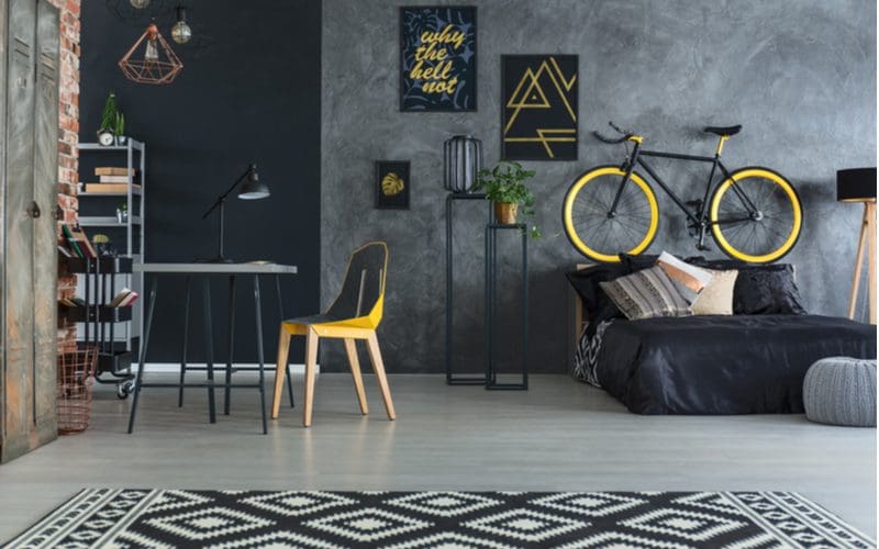 Open Concept Bedroom Office idea with a bike hanging above the bed and lots of yellow accents in the otherwise dark and drab room 