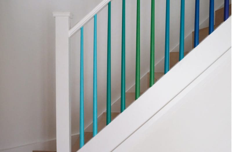 Scandinavian-style stair decorating idea featuring a white staircase with white walls and white railings with colorful spindles in green and blue colors
