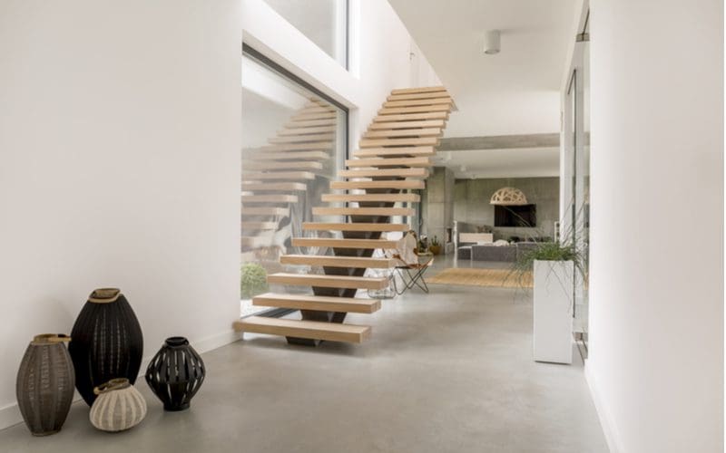 Minimalist interior design style featuring a simple concrete room with white walls and floating natural wood stairs with flower pots and vases with nothing in them as decorations in the corner