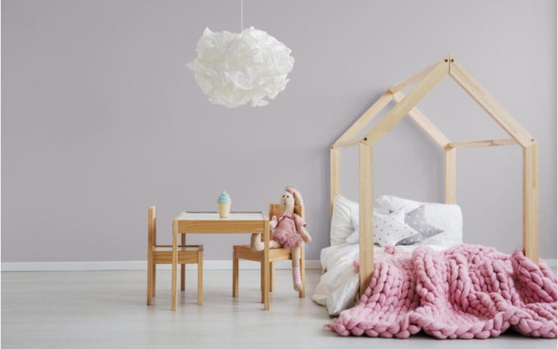 Castle bed frame made from natural wood next to a simple play coffee table below a paper chandelier for a piece on cute rooms for girls