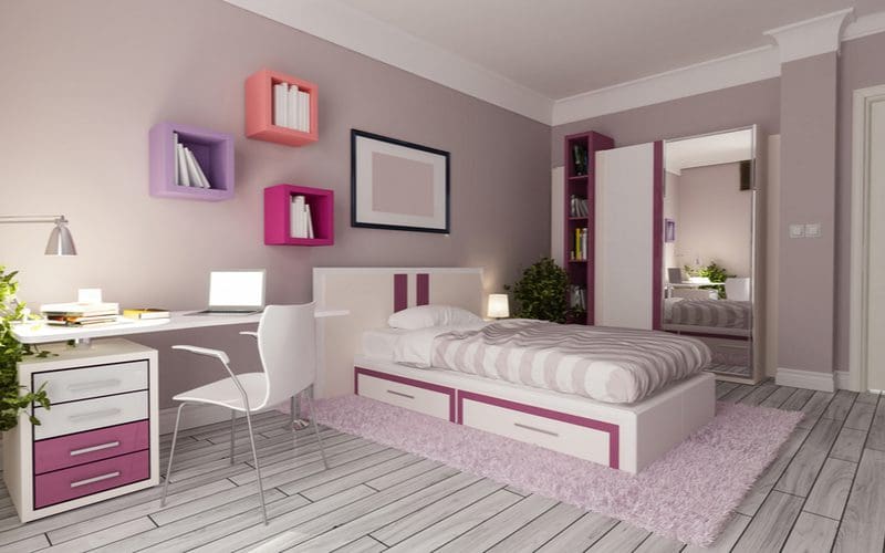 Cute girls' room with a small double storage bed with striped bedding below square floating shelves with grey tile flooring and mid-grey walls