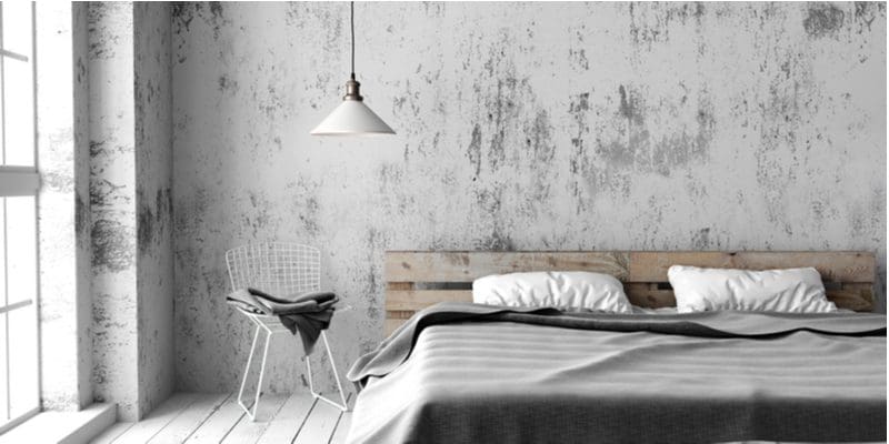 Bedroom with industrial styling and a pallet bed with concrete walls, a big open floor to ceiling window, and a hanging pendant light fixture with a white cover