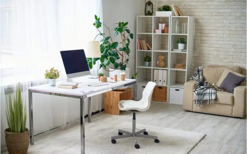 Home office design idea with modular square shelves and a white and chrome task desk in a cream-painted brick room in front of a window