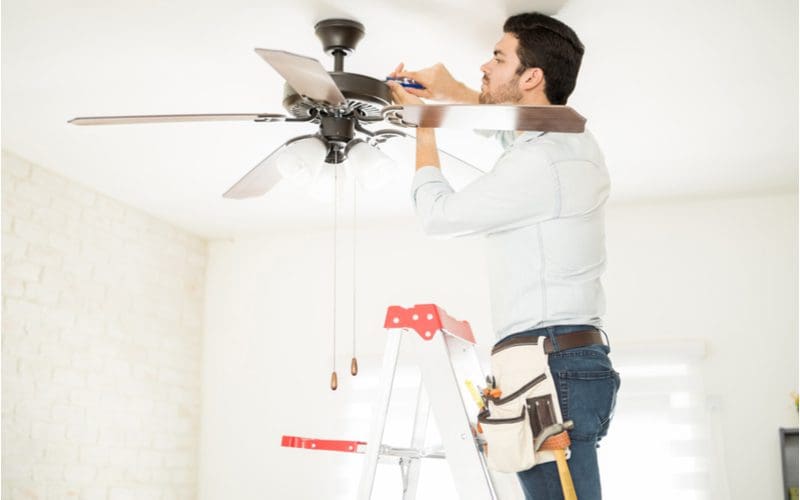 Handyman on a ladder installing a ceiling fan for a piece on ceiling fan alternative for low ceilings