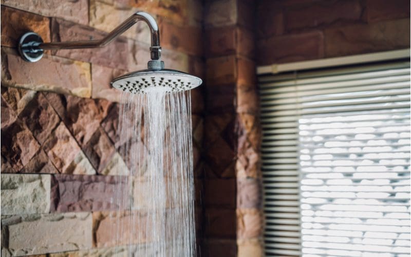 Shower head that's an average height above the ground against a natural slate tile brick wall