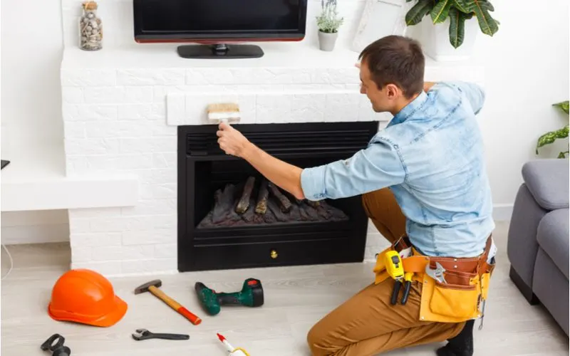 Guy installing a standard height fireplace mantle and painting the brick around it