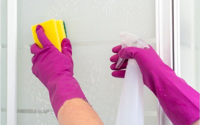 Faceless person cleaning a fiberglass shower with pink gloves and a sponge
