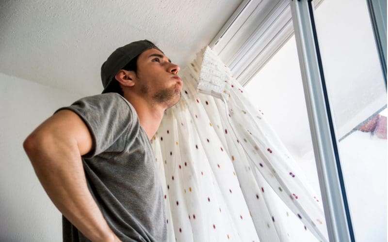 Man wearing a backwards hat holding white speckled curtains for a piece on how to hang curtains without nails