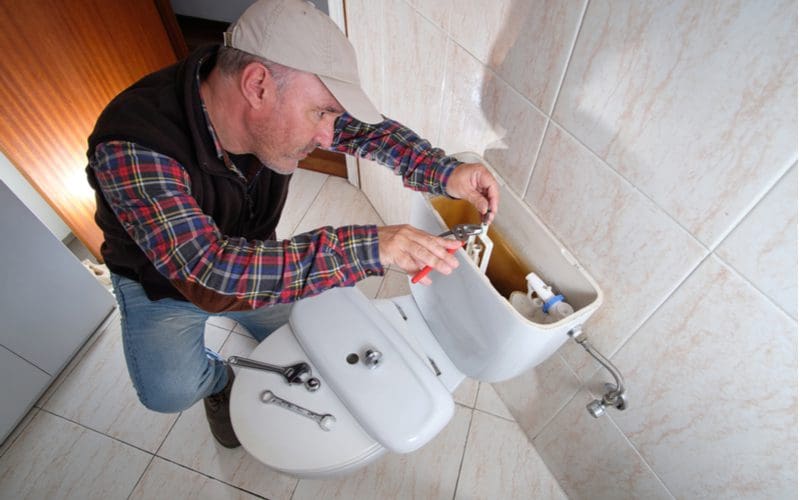 Plumber fixing a toilet that won't stop running with the lid pulled off and some parts already removed