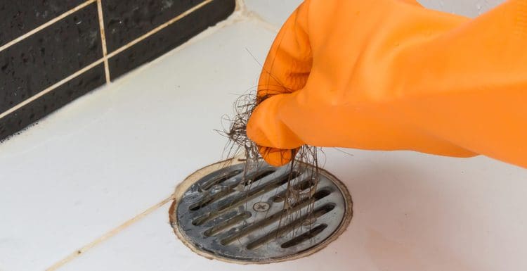 Gloved orange hand pulling hair out of a drain stopper in step 2 of how to unclog bathroom drain