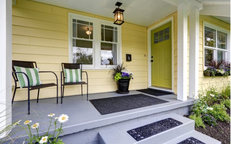 Sage Green front door color for yellow house next to a grey porch