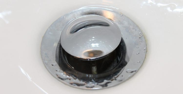 Featured image for a piece titled how to remove a sink stopper featuring a close-up shot of a chrome stopper on a porcelain sink