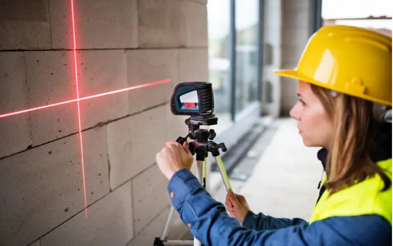 Woman using a laser level on a brick block wall for a piece on types of measuring tools