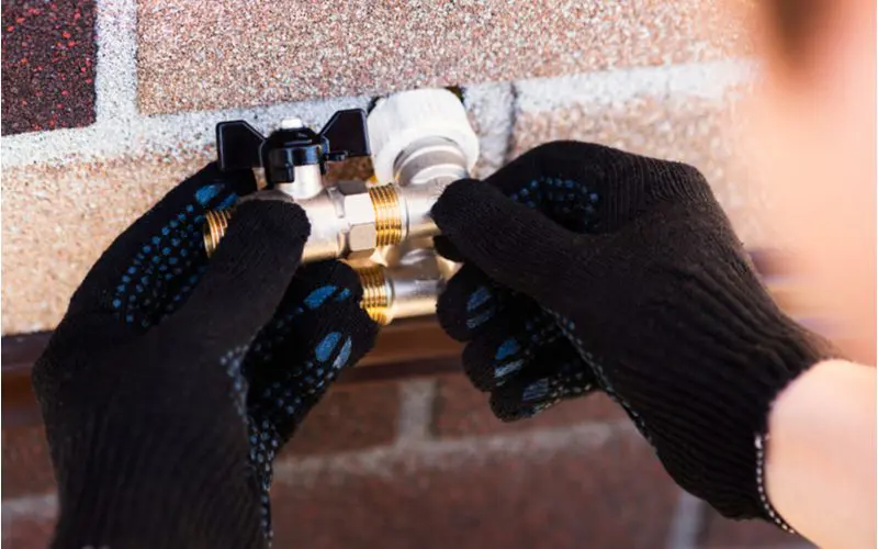Guy replacing one of the parts of an outdoor faucet with black gloves