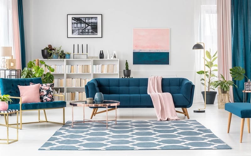 Living room with blue sofa and pink details like pillows and blanket and wall decor
