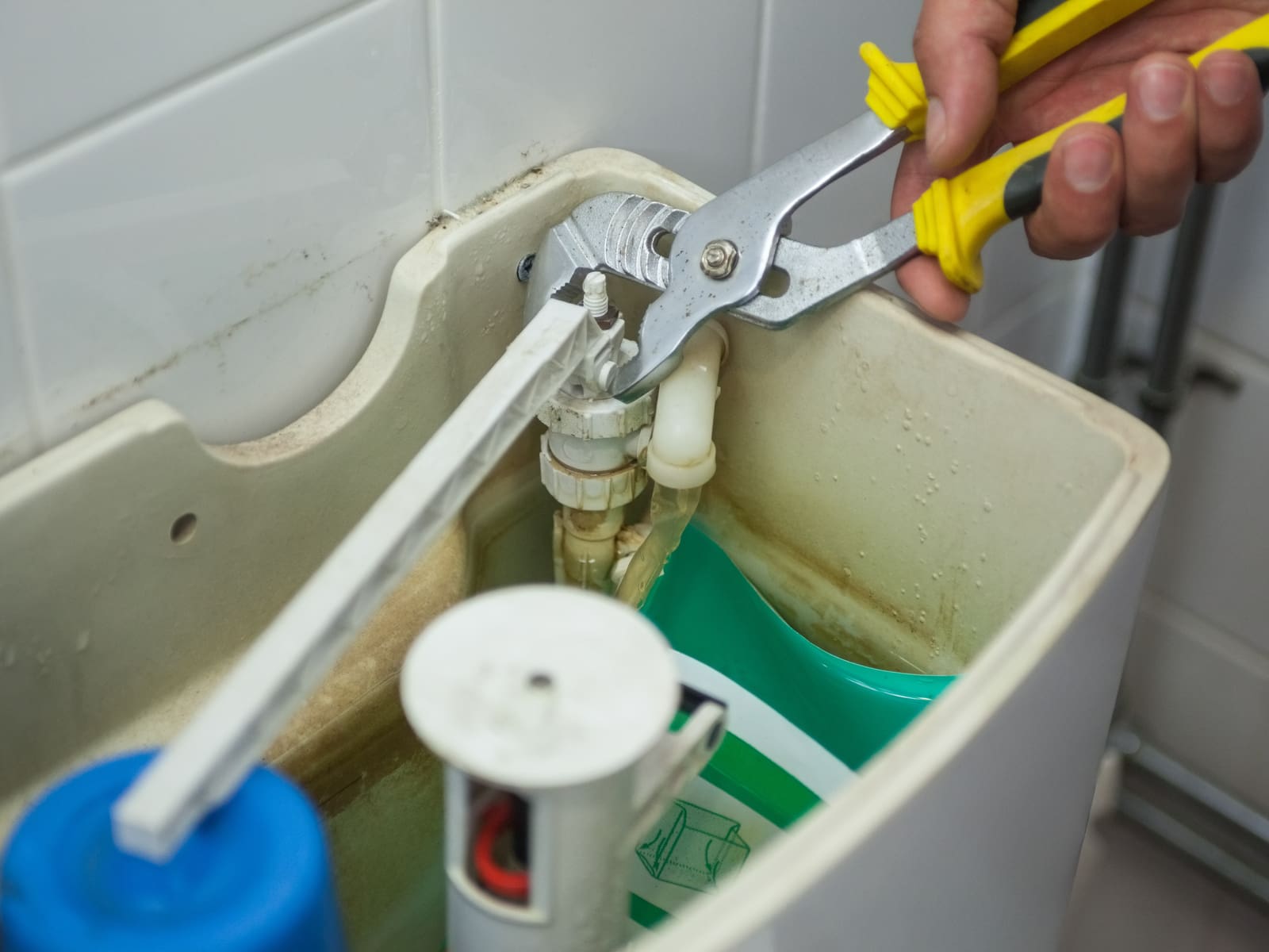 Close up of hand repairing toilet with pliers