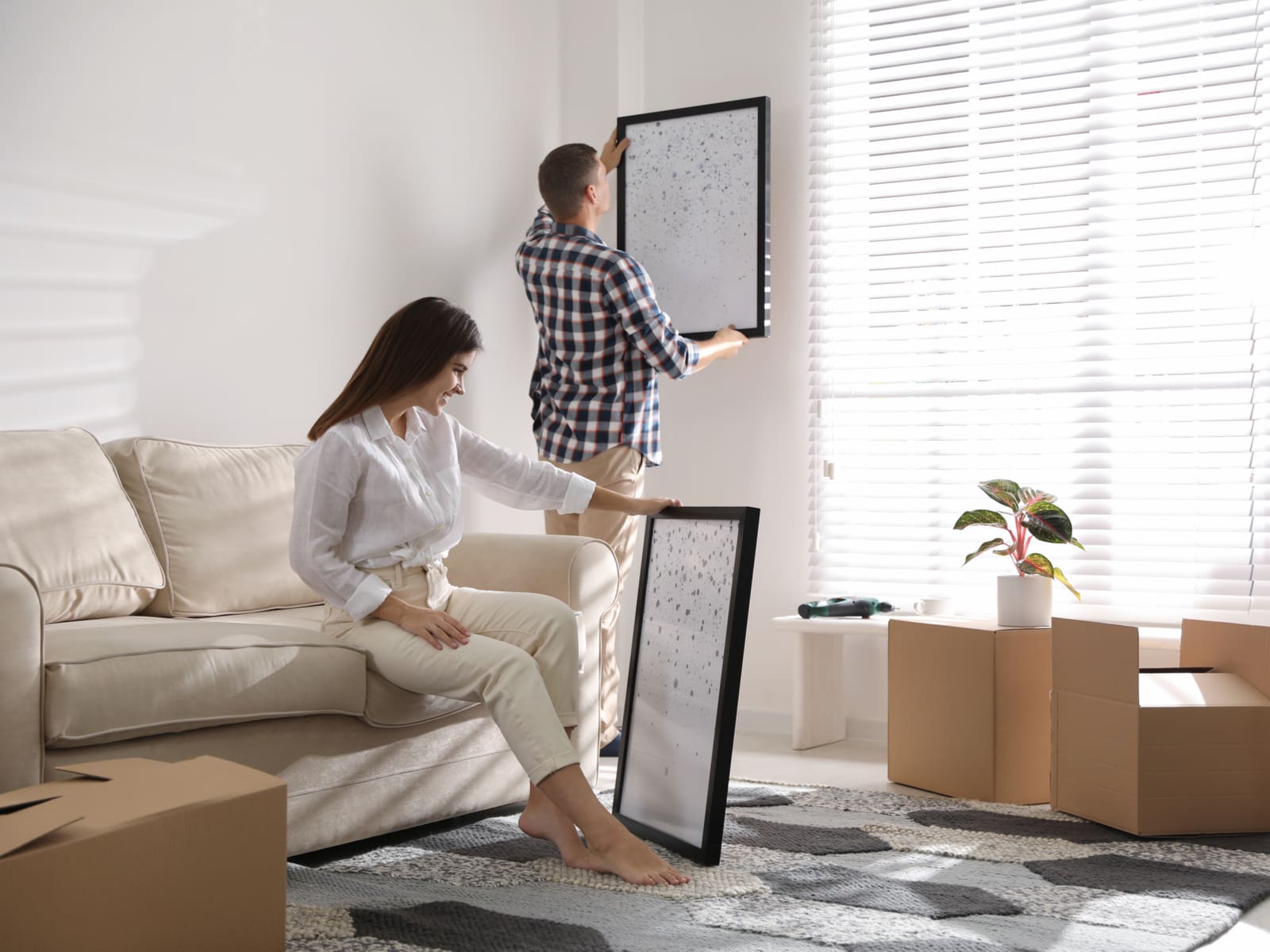 Two people decorating a living room with colors that go with white, including beige and greys