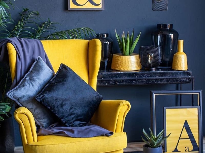 Mustard yellow chair and navy blue pillows with dark blue walls