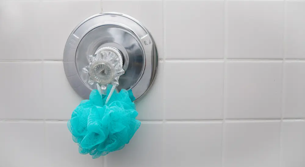Loofah hanging from a shower handle in a white tiled shower