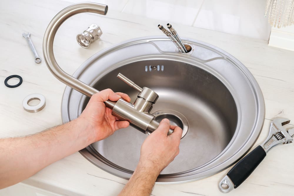 Plumber taking apart a kitchen faucet and laying other kitchen sink parts next to the sink