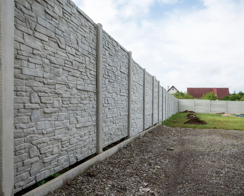 A unique types of fence made of precast concrete running alongside a backyard