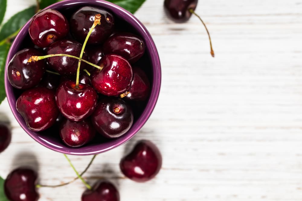Black Tartarian Cherry, one of the best types of cherries, pictured in a violet bowl on a wooden table