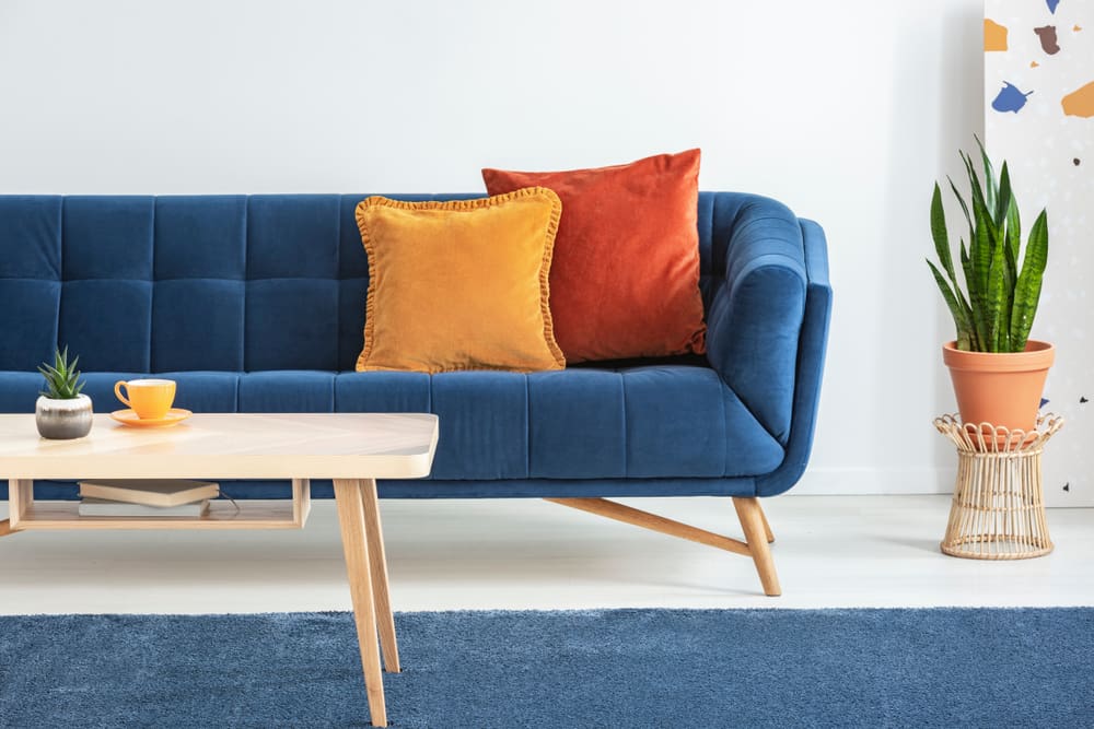Image of a blue sofa and a yellow pillow, two colors that go best with burnt orange