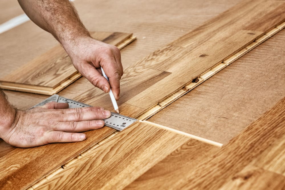Craftsman marking a measurement on a hardwood floor for a piece on the types of wood flooring