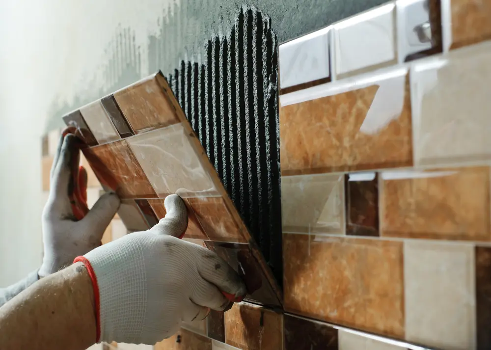 Guy laying ceramic tiles, some of the best types of bathroom tiles, on a wall