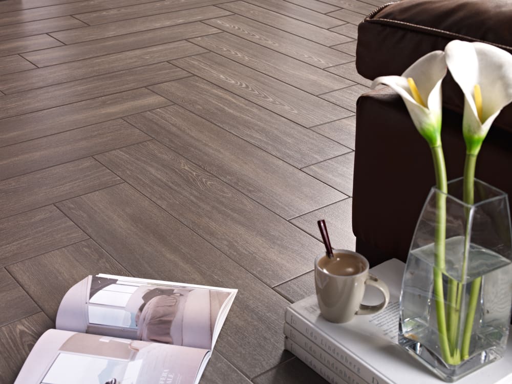 Ceramic floor tile pictured in a herringbone pattern made from a grey wood look tile