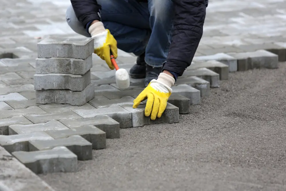 Guy laying stone pavers on a patio or walkway with his hands and white and yellow gloves